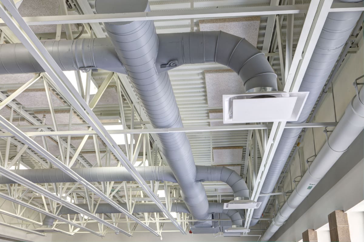 Industrial HVAC ducts installed on a ceiling with metal beams.