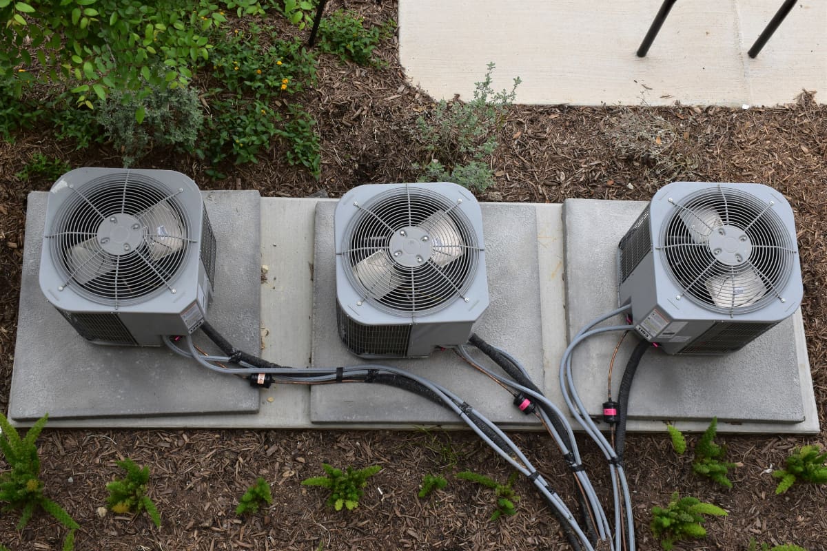 Three outdoor air conditioning units connected with cables and chains.